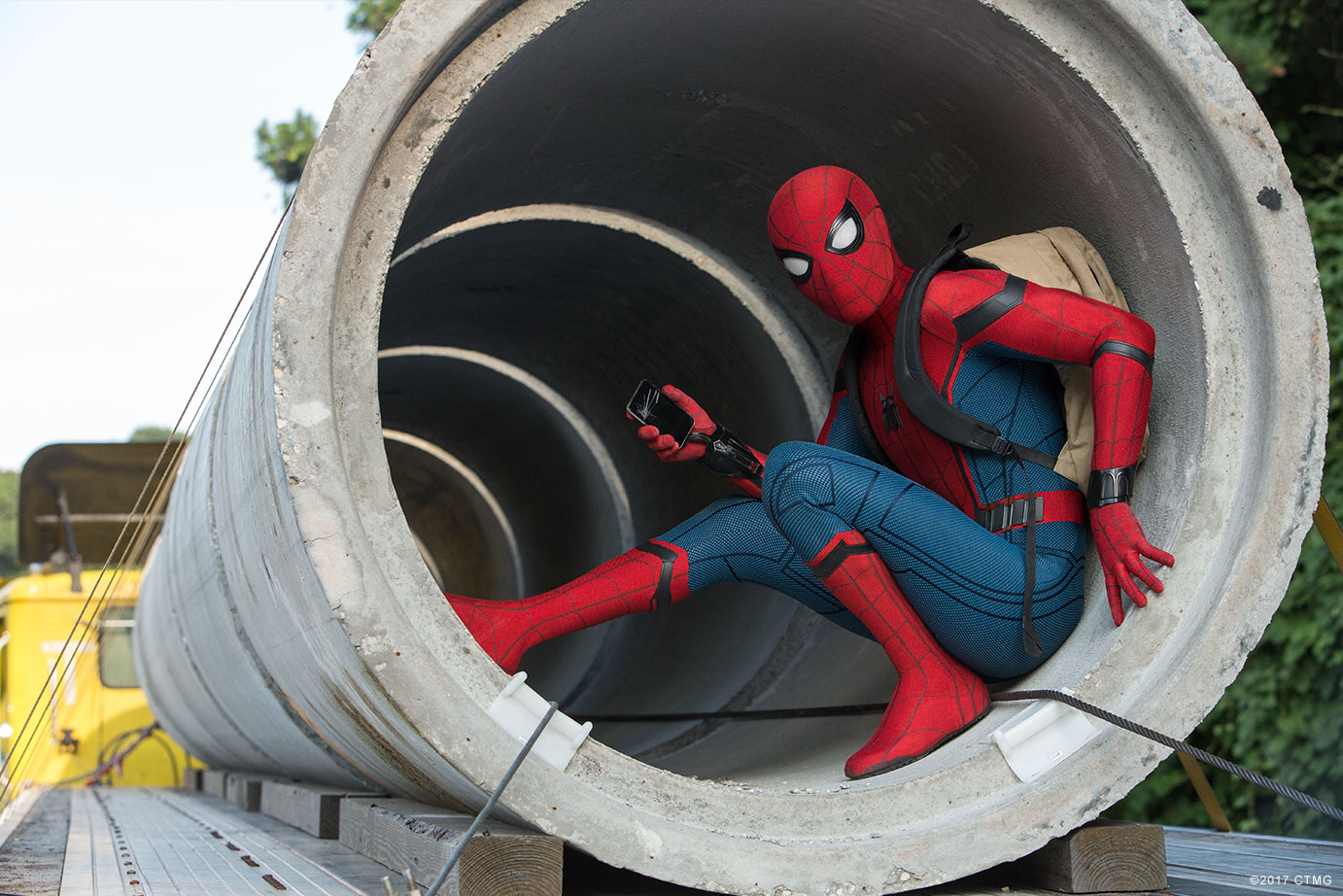 Spider-Man hiding inside a pipe with his cellphone and backpack in SPIDER-MAN HOMECOMING