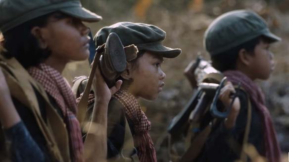 A scene of children dressed as soldiers holding guns on their backs in Angelina Jolie's film FIRST THEY KILLED MY FATHER.