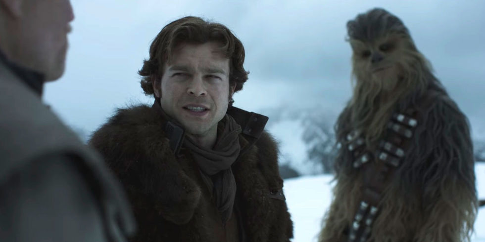 Alden Ehrenreich in Solo: A Star Wars Story looking skeptically at Woody Harrelson while Chewbacca stands in the background looking the same way with his head tilted.