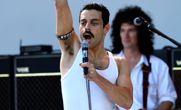 Rami Malek as Freddie Mercury in the film Bohemian Rhapsody singing at Live Aid with one arm in the air