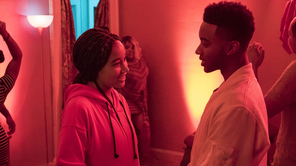 Amandla Stenberg and Algee Smith in the reddish glow of a party looking at each other and smiling in the film The Hate U Give