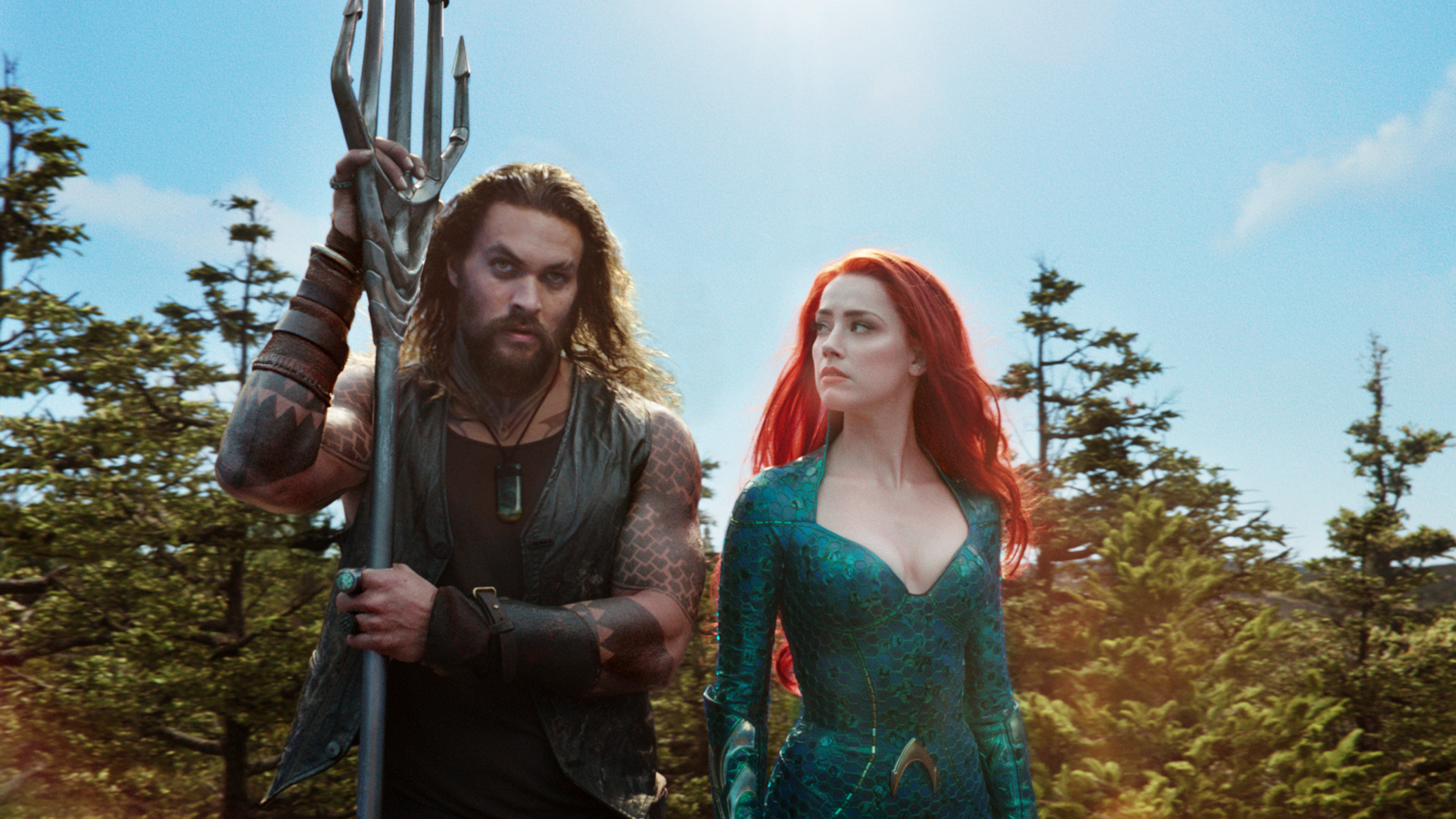 Jason Mamoa leaning on his trident and Amber Heard looking intently to him on the left in the movie Aquaman