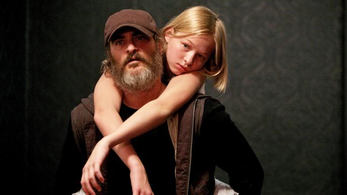 Joaquin Phoenix and carrying Ekaterina Samsonov on his back while her arms are draped over his shoulders in the movie You Were Never Really Here