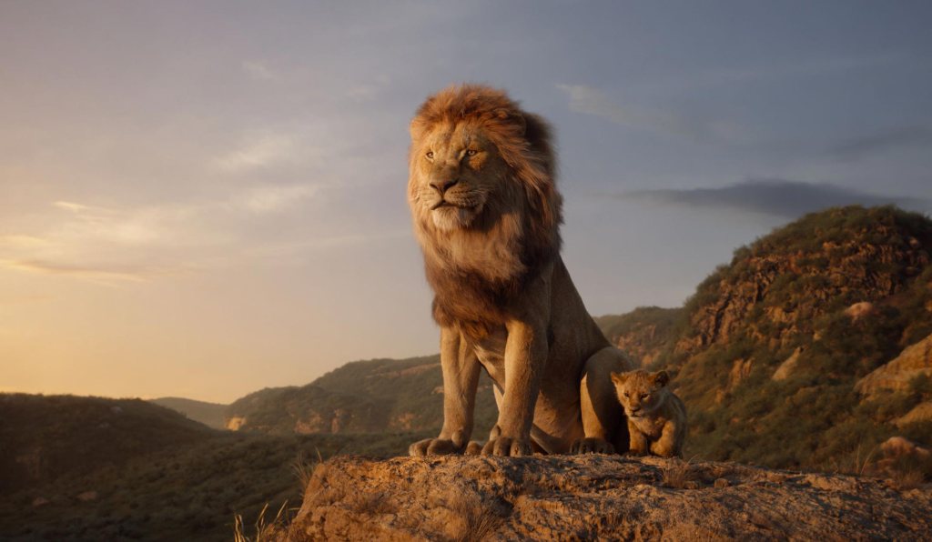 A male lion standing on a hilltop majestically with a lion cub in the 2019 movie The Lion King