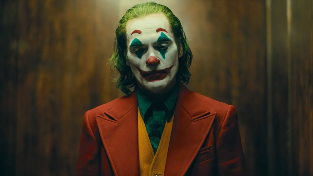Joaquin Phoenix in the movie Joker wearing his makeup in a suit pondering something in an elevator