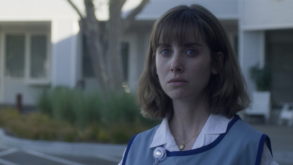 Alison Brie looking sad wearing a craft store smock in the movie Horse Girl