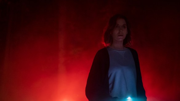 Alison Brie stands against red fog holding her cellphone light in the movie The Rental