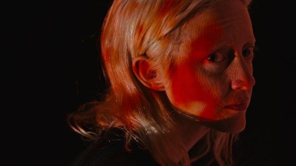 Andrea Riseborough looking worried and cast in an orange glow in the movie Possessor.