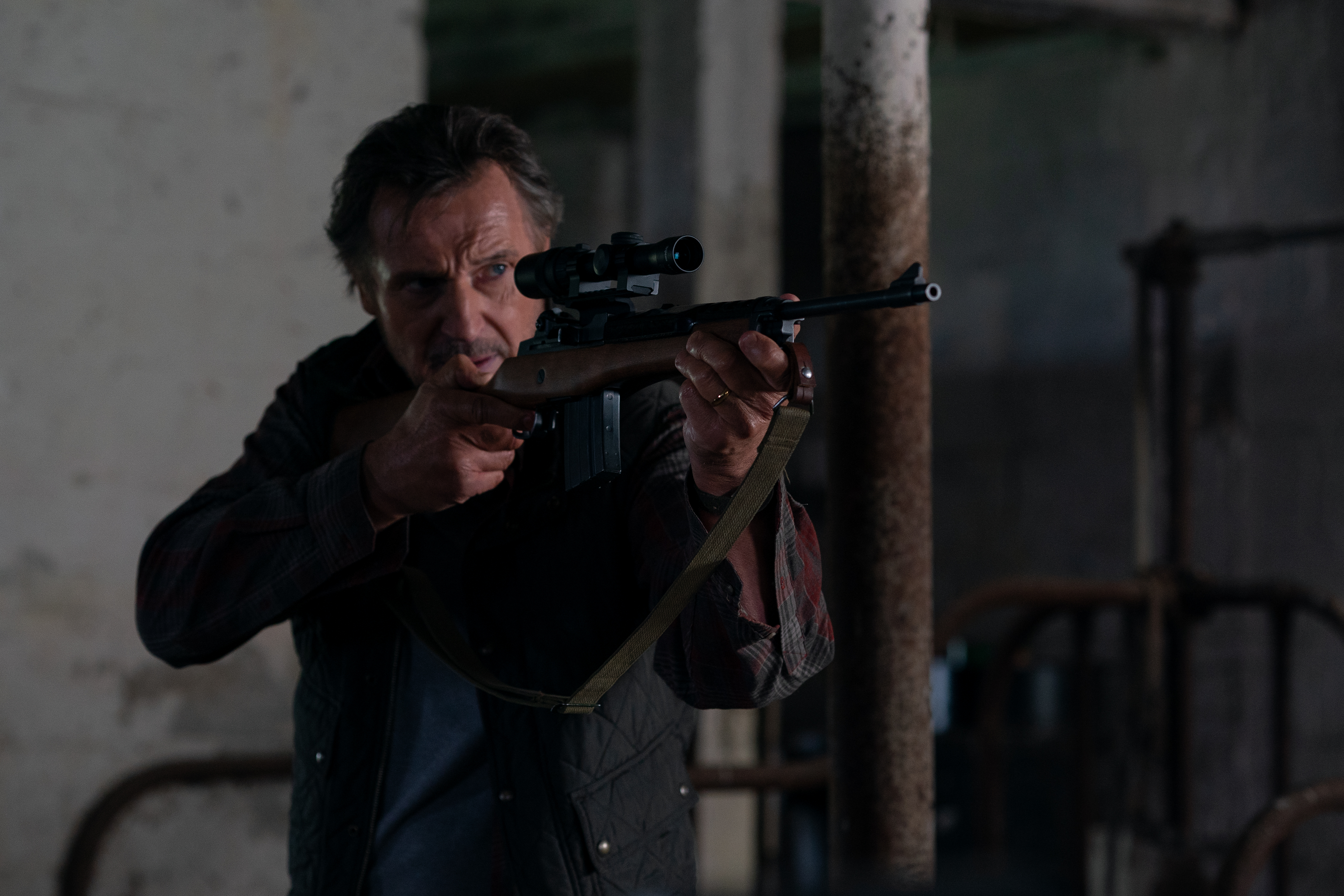 Liam Neeson holds a rife and looks into the sight in the movie The Marksman