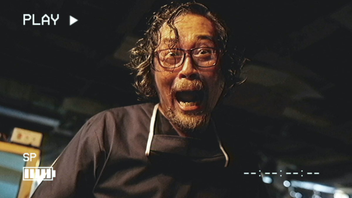 An Asian man with glasses laughing maniacally as he's being recorded through a video camera display in the horror anthology V/H/S/94