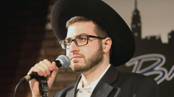 Orthodox Jewish comedian Daniel Finkelstein holds a microphone in the documentary A Jew Walks into a Bar