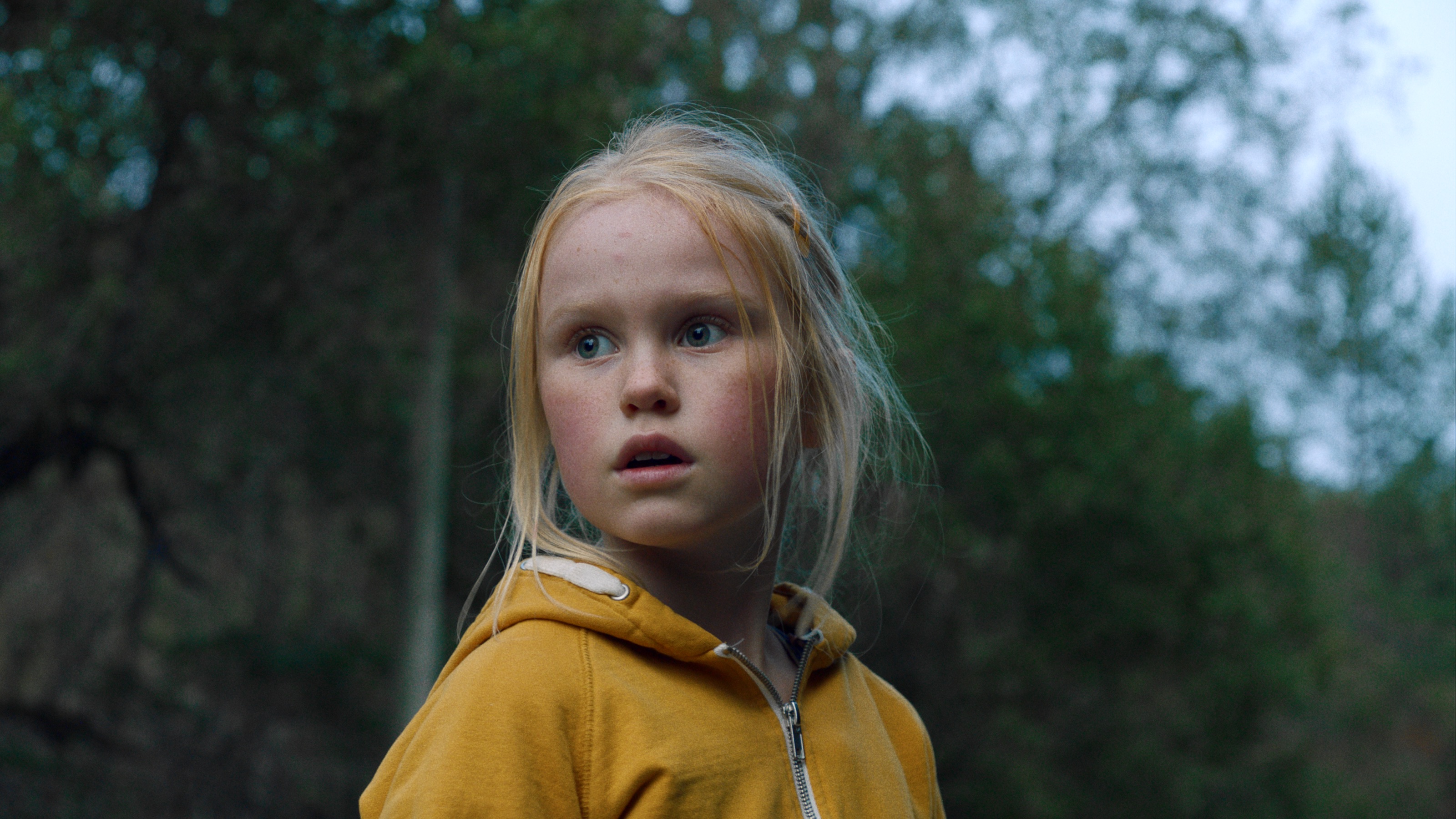 A little blond girl in a yellow jacket looks frightened in the Norwegian movie The Innocents.
