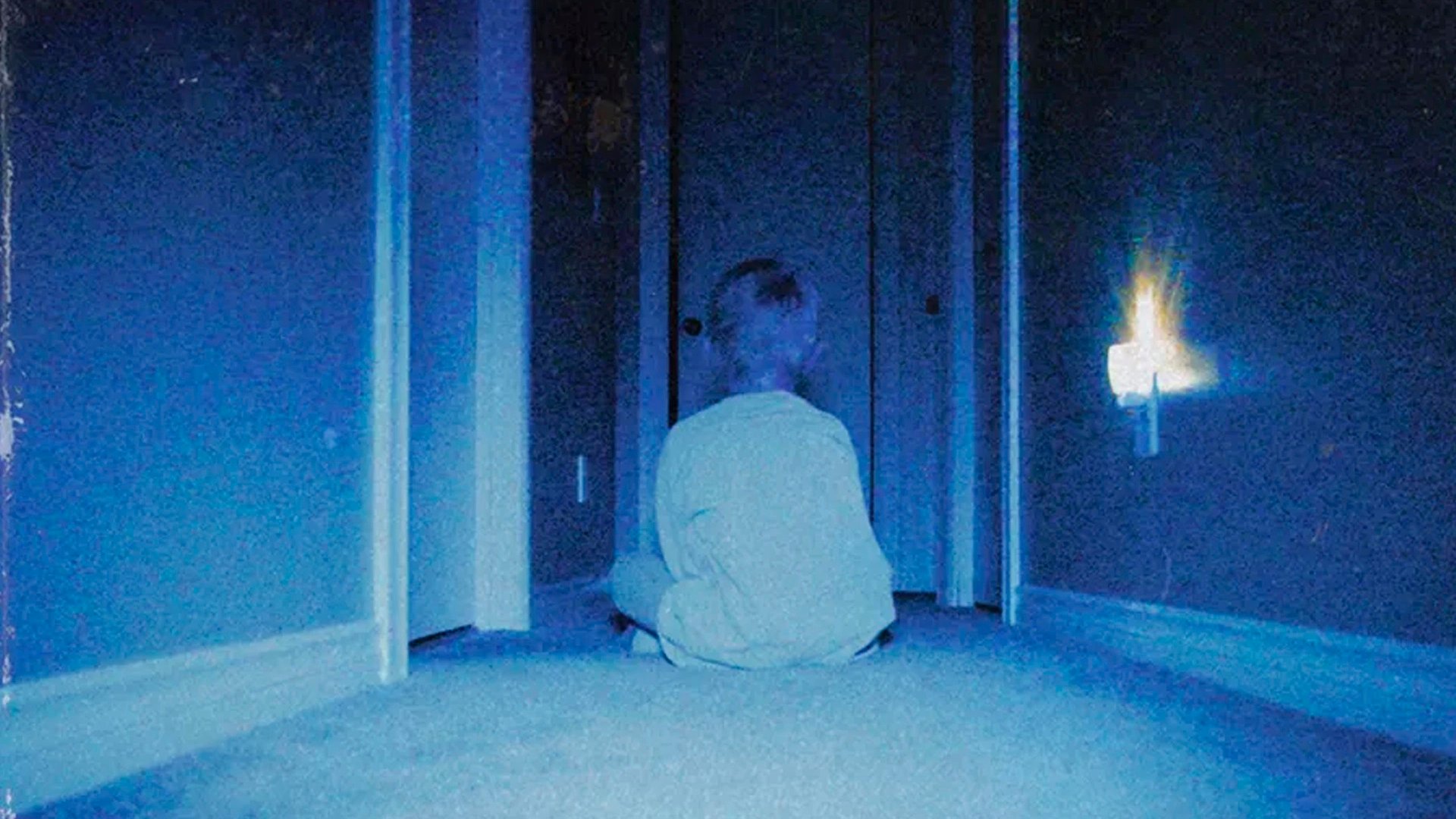 A seated child sits with their back turned in a dark hallway in the movie Skinamarink.