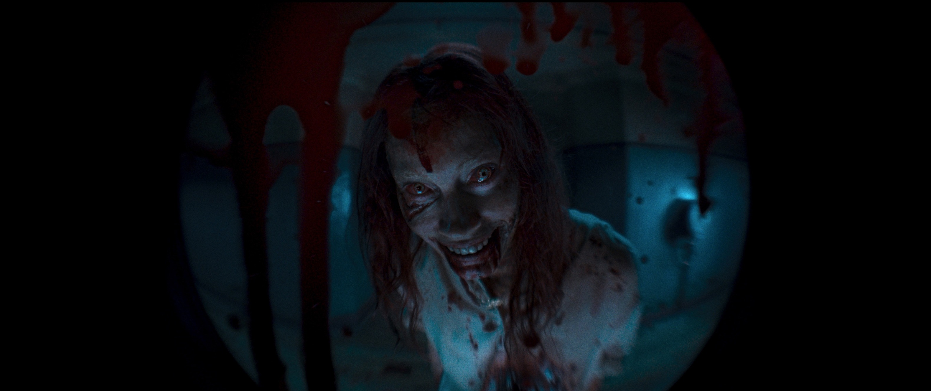 Alyssa Sutherland as a Deadite grins and stares creepily through a bloody peephole in Evil Dead Rise.