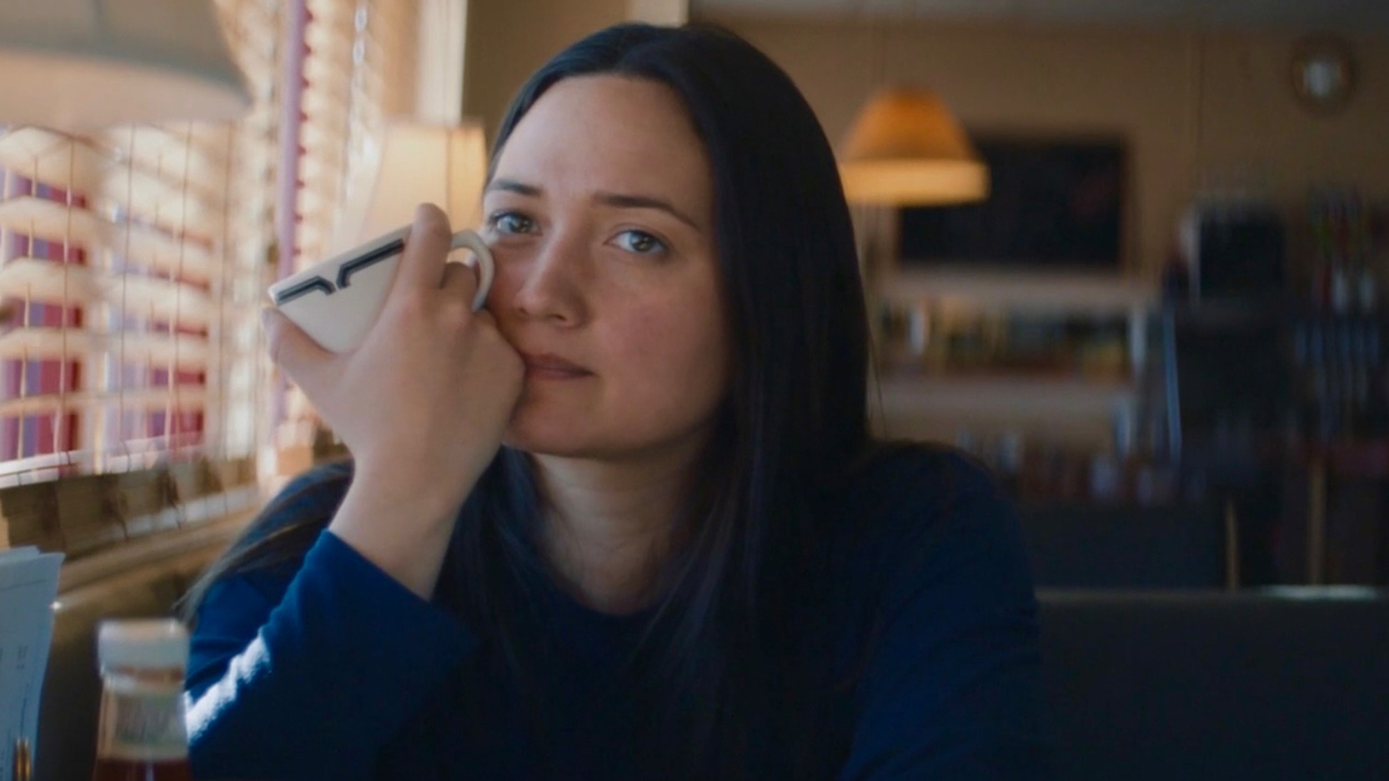 Lily Gladstone sits holding a coffee cup to her face in the film The Unknown Country.